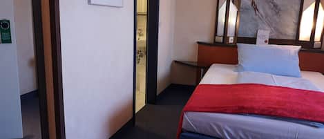 A hotel room with a bed, a nightstand, a painting, and a door leading to a bathroom.