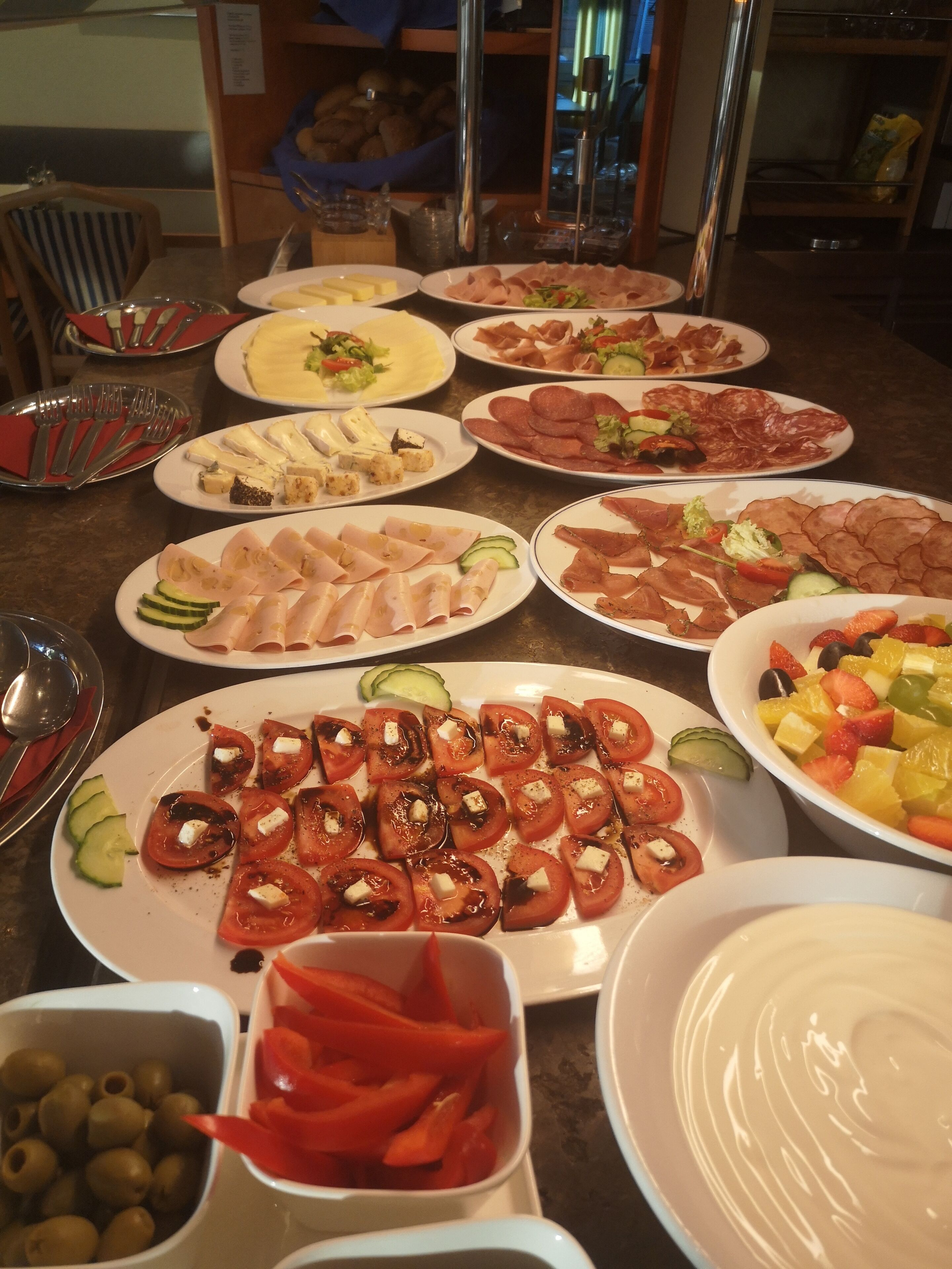 Ein Buffet mit verschiedenen Speisen, darunter Tomatenscheiben, Käse, Fleisch und einem Obstsalat.