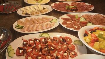 Ein Buffet mit verschiedenen Speisen, darunter Tomatenscheiben, Käse, Fleisch und einem Obstsalat.