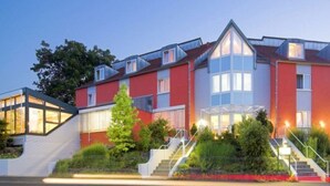 A multi-story hotel with a red facade, large windows, and a central staircase. - Main Hotel Eckert (Margetshoechheim)