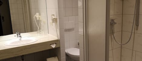 A bathroom with a sink, mirror, toilet, and shower.
