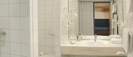 A bathroom with white tiles, a sink, a mirror, and a toilet.