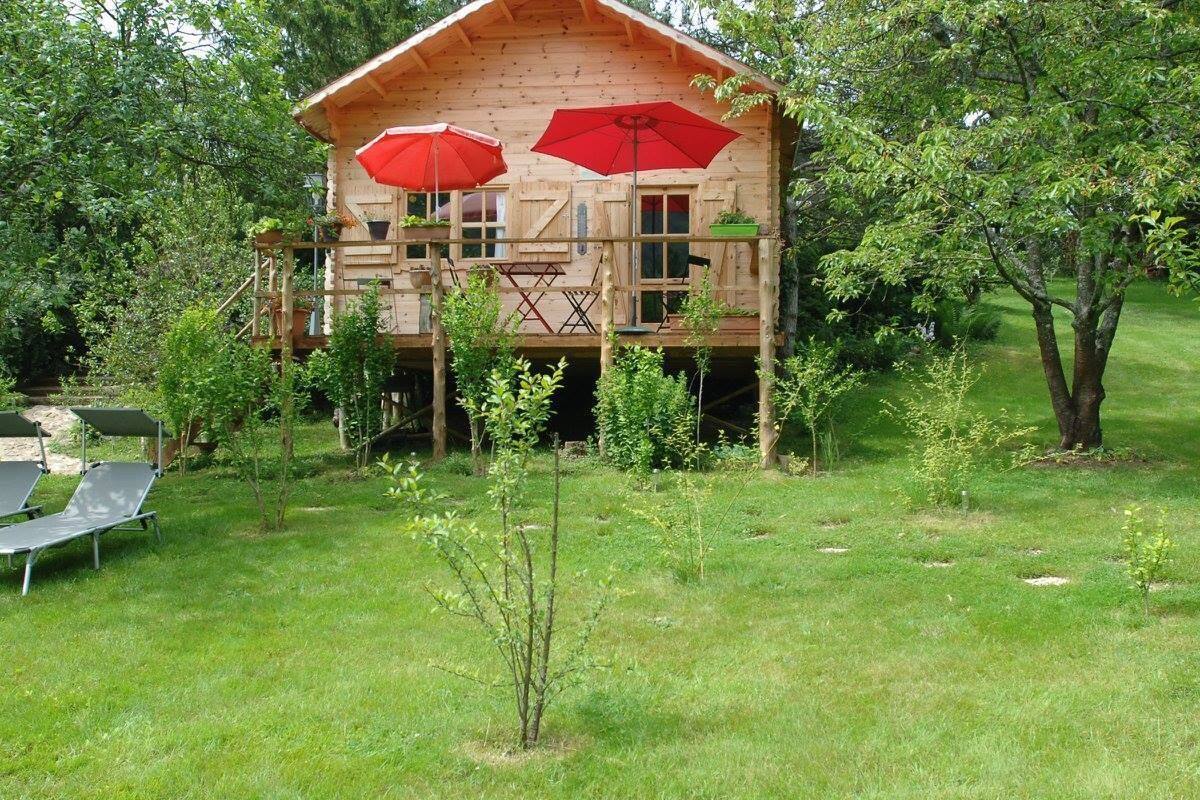 A wooden cabin with a balcony, red umbrellas, and a small garden area.