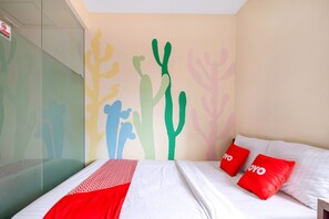 A hotel room with a bed, two red pillows, a white bedspread, and a wall with colorful cactus silhouettes. - Capital O 1121 Orienchi 2 (Jakarta)