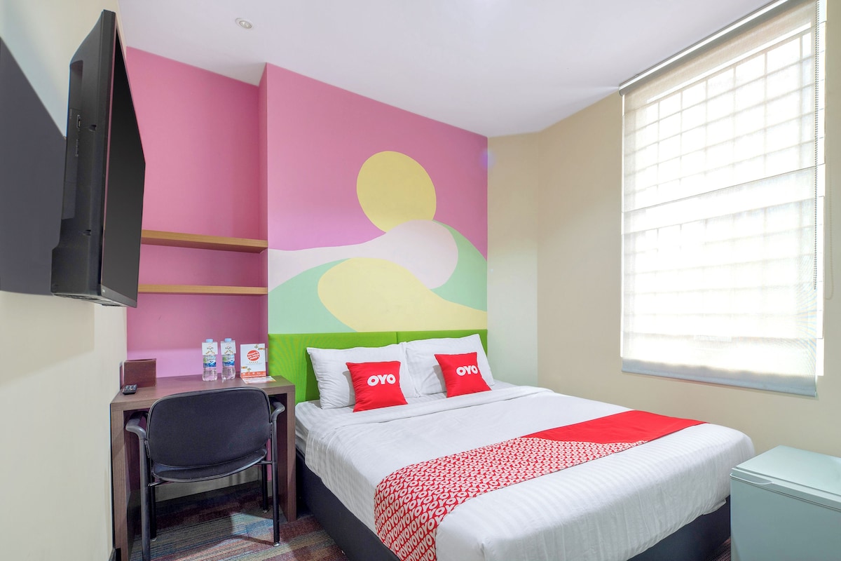 A hotel room with a bed, a desk, a chair, a TV, and a window with blinds.