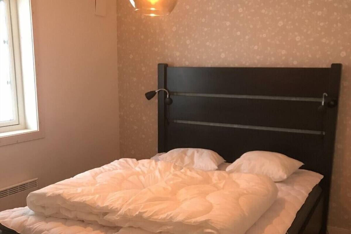 A bedroom with a bed, a hanging light fixture, and a window.