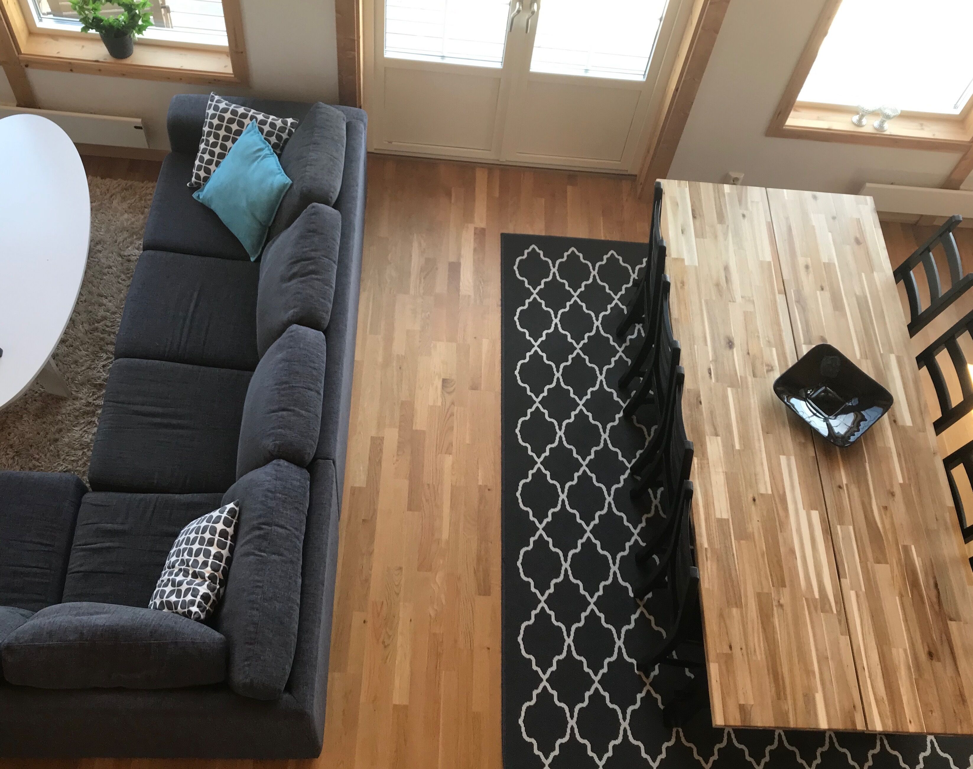 A modern living room with a grey sofa, patterned cushions, a wooden dining table, and a black and white patterned rug.