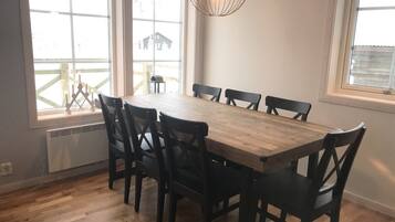 A dining area with a wooden table and six chairs, large windows with a view of a building outside, and a hanging light fixture.