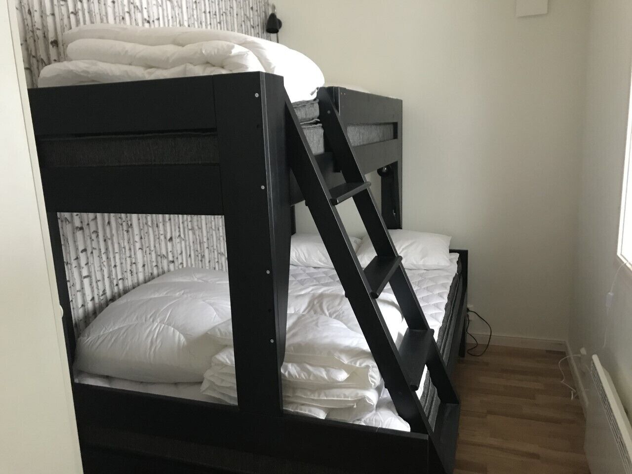 A bunk bed with a ladder, white bedding, and a wooden floor.
