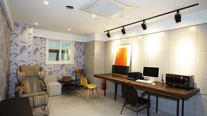 A modern office space with a desk, two chairs, a massage chair, a small table with a basket, and a large window. - Hotel No25 Songdo (Incheon)