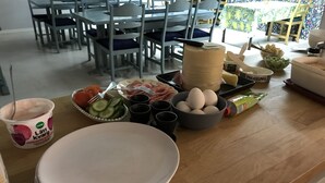 Een eetgedeelte met tafels en stoelen, een toonbank met etenswaren en bestek, en een wand met een patroon in de achtergrond.