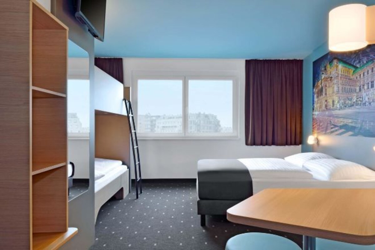 A hotel room with a bunk bed, a desk, and a window with curtains.