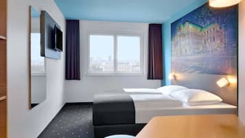 Habitación de hotel con cama, escritorio, silla, ventana con cortinas, un cuadro en la pared y televisor montado en la pared.