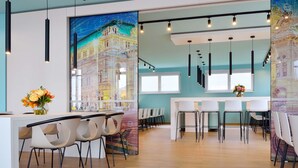 Een modern interieur met een centraal gelegen eethoek, witte stoelen en een lange tafel. Er zijn hanglampen en een muurschildering op de muur.