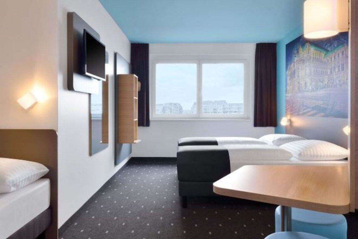 A hotel room with a bed, a desk, a chair, a sofa, a window, and a painting on the wall.