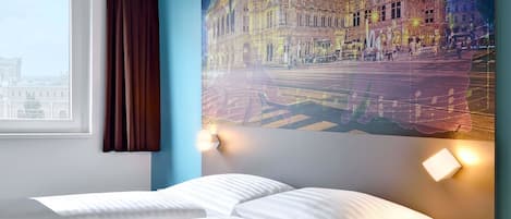 Een hotelkamer met een bed, nachtkastje, een wandlamp en een groot raam met gordijnen.