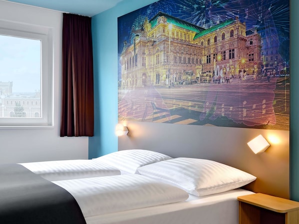 Een hotelkamer met een bed, nachtkastje, een wandlamp en een groot raam met gordijnen.