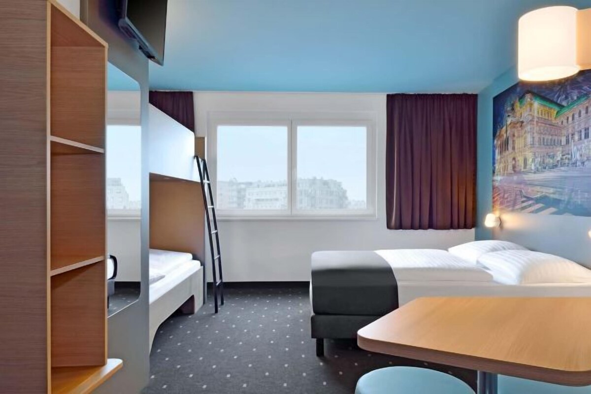 A hotel room with a bunk bed, a desk, and a window with curtains.