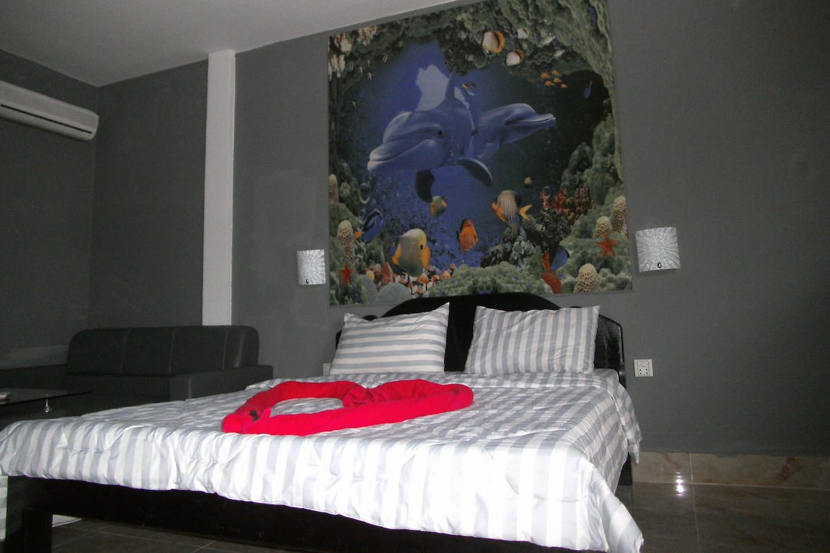 A bedroom with a bed, a red heart-shaped object on the bed, and a large wall mural of dolphins and fish.