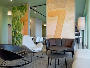 Un área de estar moderna con disposición de asientos, un mural grande en la pared y una escalera que sube a otro nivel.