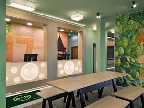 Zona de recepción de un hotel B&B con un amplio ventanal que muestra un edificio tradicional, un mostrador de recepción y un área de estar con mesas y sillas.