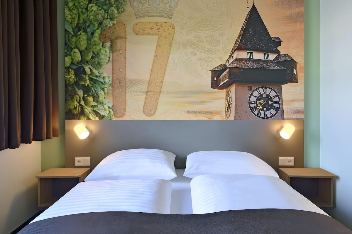 Une chambre d’hôtel avec un lit, deux tables de chevet, une horloge murale et un grand chiffre « 17 » peint sur le mur.