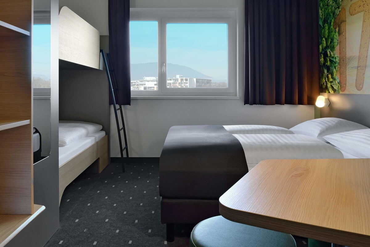 Habitación de hotel con literas, un escritorio y vistas a edificios a través de la ventana.