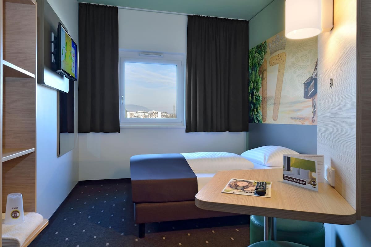 Une chambre d’hôtel avec un lit, un bureau, une fenêtre et une vue sur la ville.