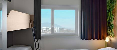 Habitación de hotel con cama, escritorio, silla, ventana con cortinas y lámpara de pared.