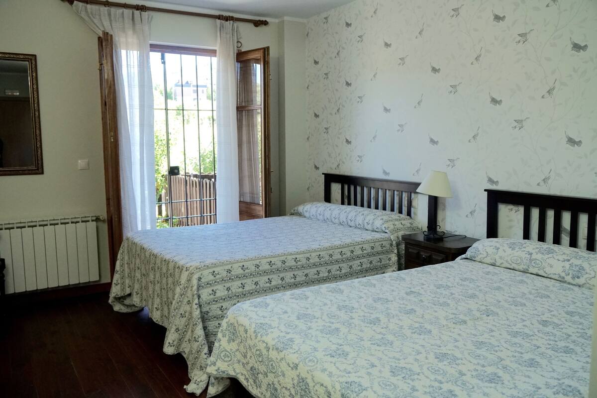 Un dormitorio con dos camas, una ventana con cortinas, un radiador y una pared con papel tapiz de mariposas.