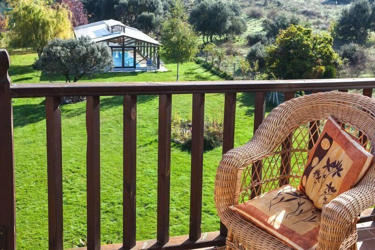 Una silla de mimbre con cojines estampados en un balcón con vistas a un césped verde y exuberante y un pequeño edificio con techo de vidrio.