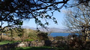A stone wall with a grassy area and a view of a body of water and mountains in the distance. - Westport Coastal Lodge (Westport)