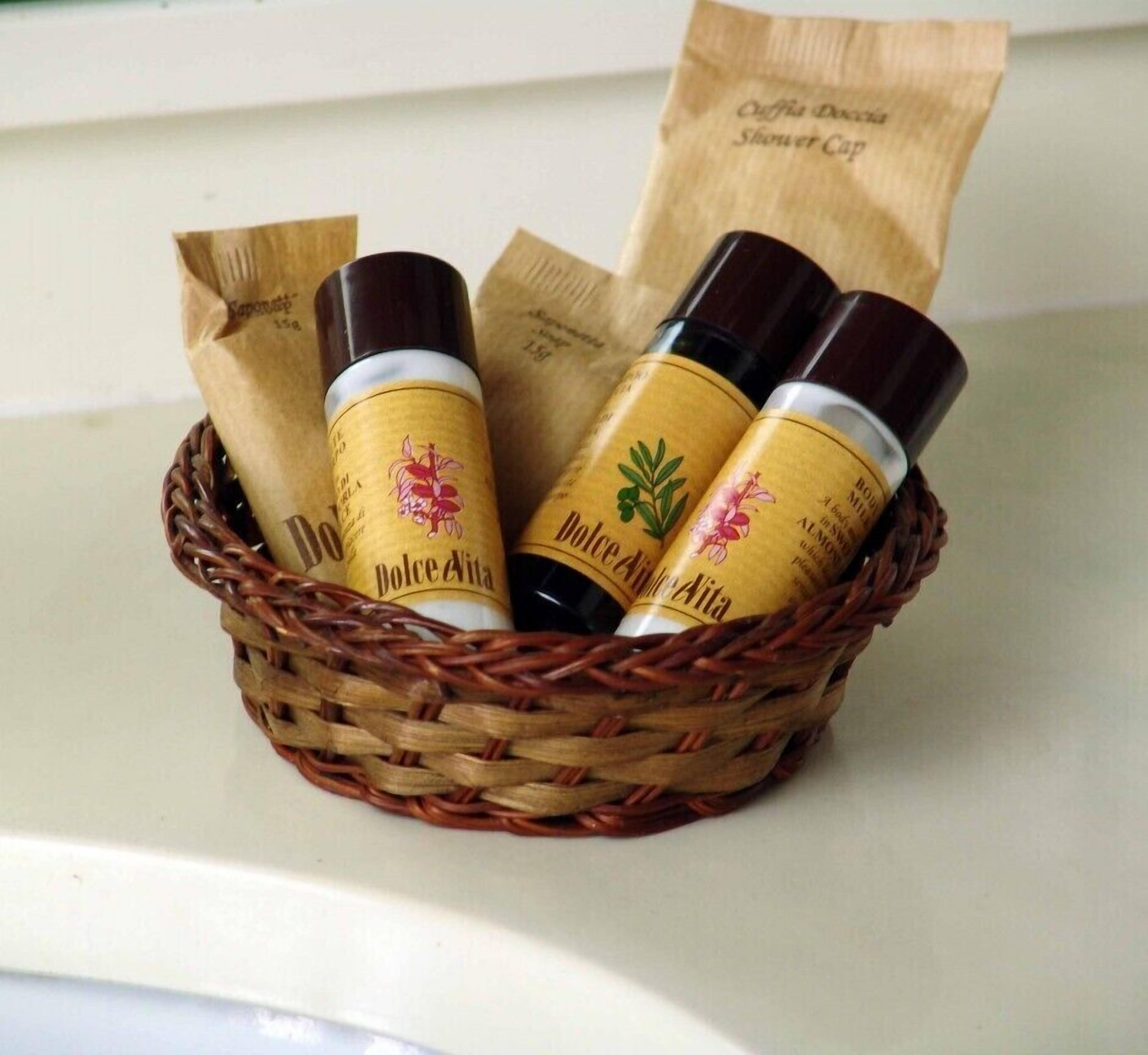 A wicker basket containing three bottles of Dolce Vita shower cap soap, with a paper bag labeled 'Olfia Doccia Shower Cap' in the background.