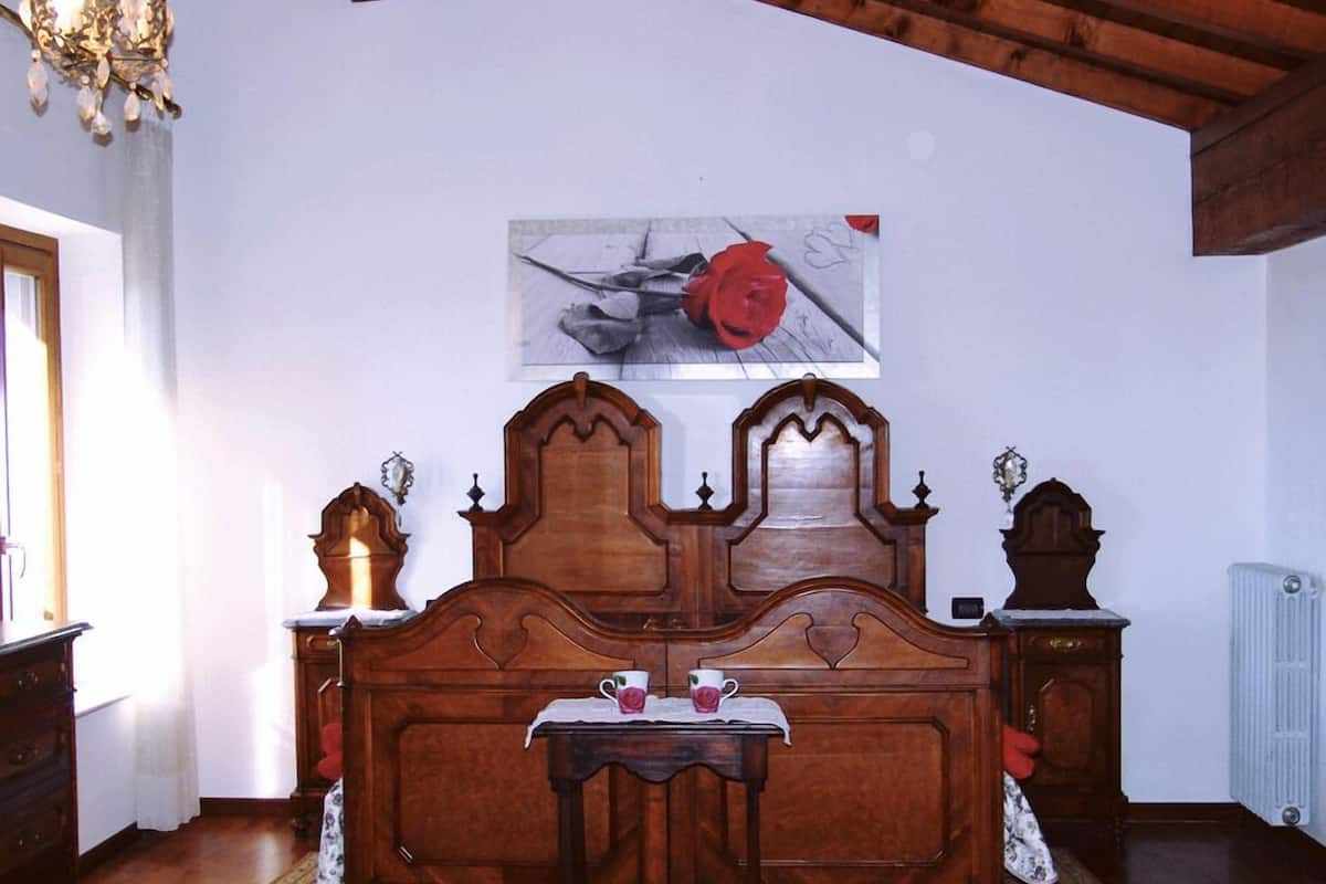 Ein Schlafzimmer mit einem hölzernen Bett, einem kleinen Tisch mit einer Tasse und einer Rose, sowie einem Bild an der Wand.