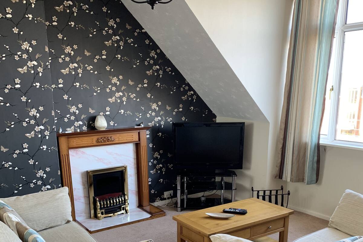 Una sala de estar con dos sofás, una chimenea, un televisor y un ventanal con cortinas.