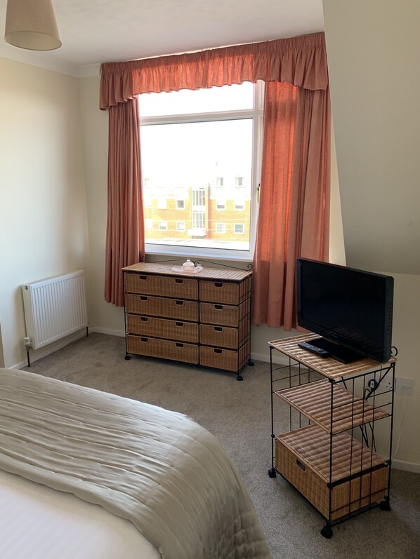 Une chambre à coucher avec un lit, une commode, un téléviseur posé sur un meuble et une fenêtre avec des rideaux.