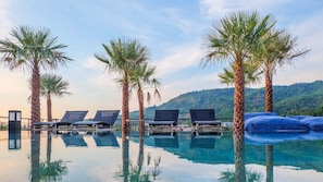 Zona piscina con lettini e palme, riflesse nell'acqua.