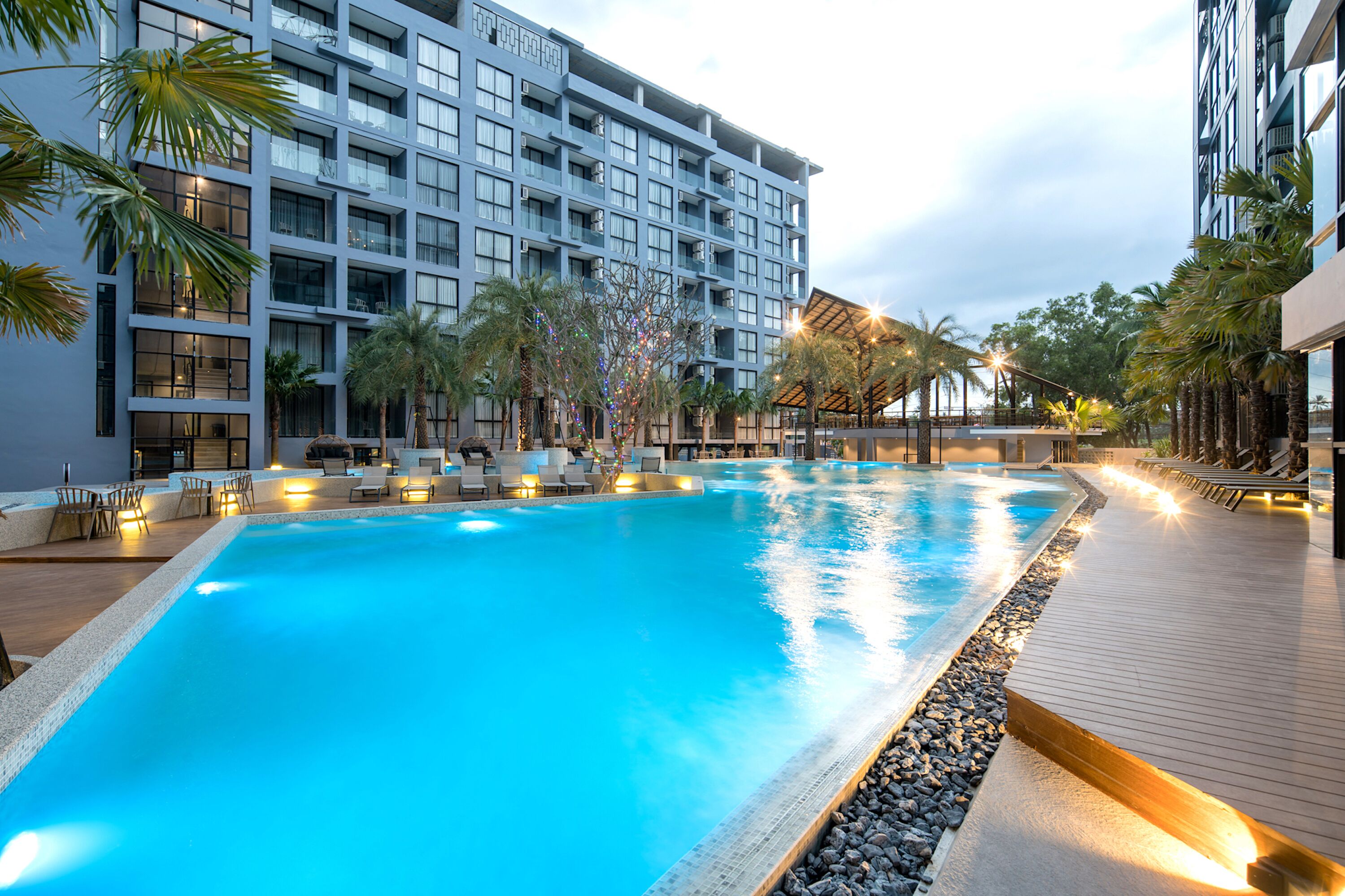 A swimming pool with lounge chairs and palm trees, surrounded by a modern hotel building.