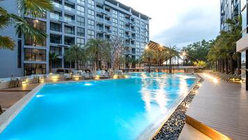 A swimming pool with lounge chairs and palm trees, surrounded by a modern hotel building.