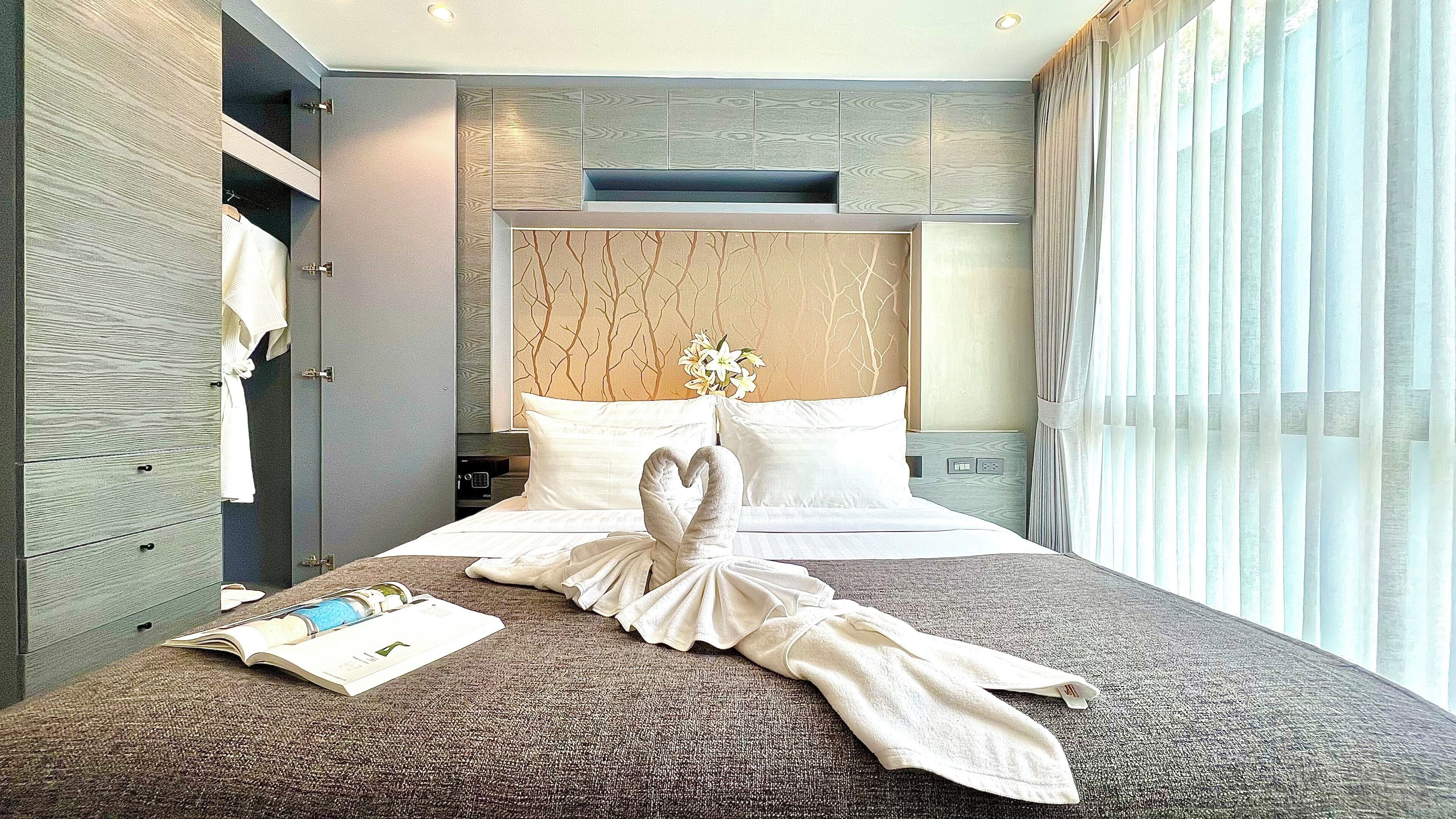 Une chambre d’hôtel avec un grand lit, une tête de lit en bois, une table de chevet et une fenêtre avec des rideaux.