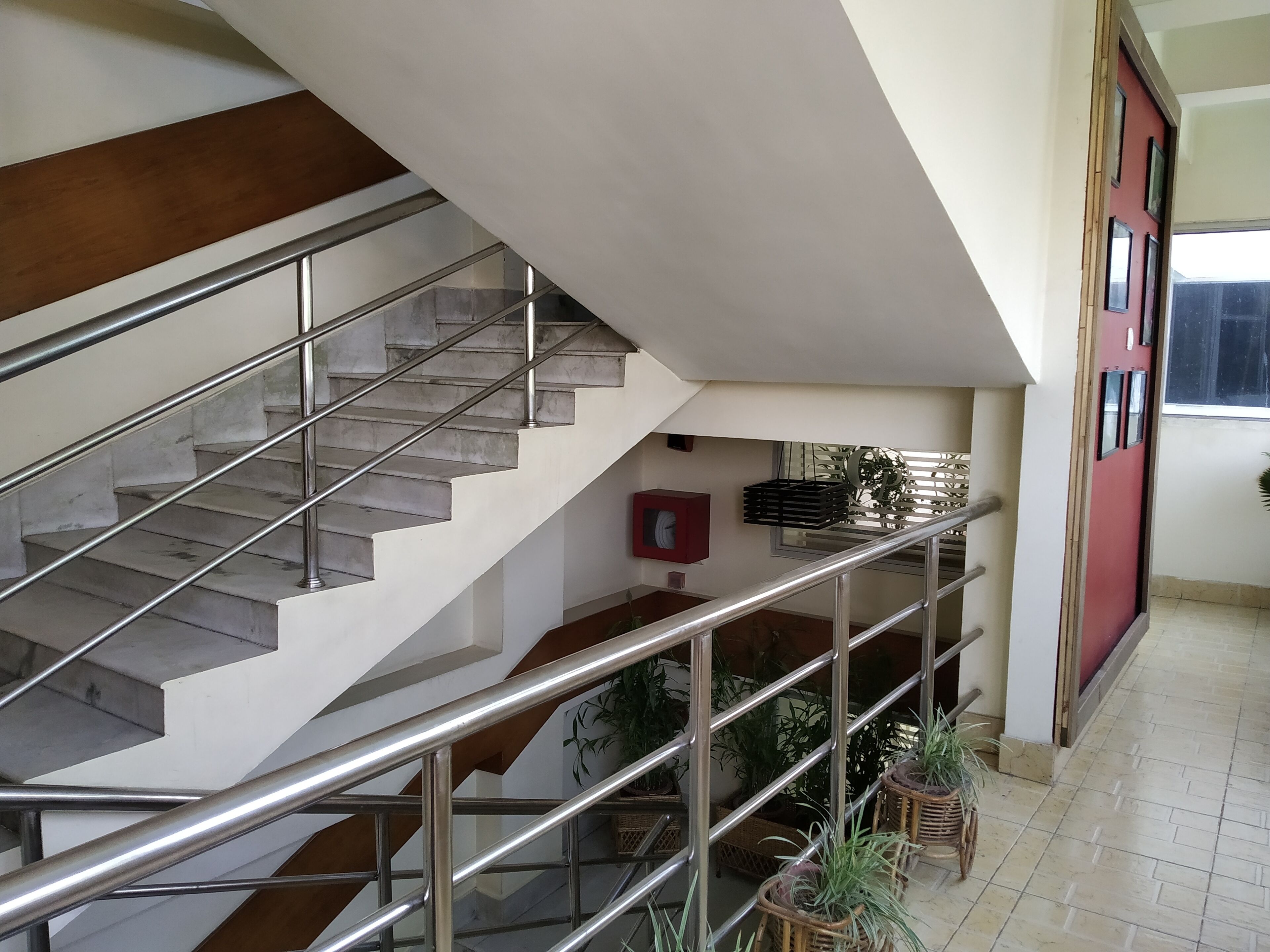 Una escalera con barandillas de metal, una puerta roja y plantas en macetas.