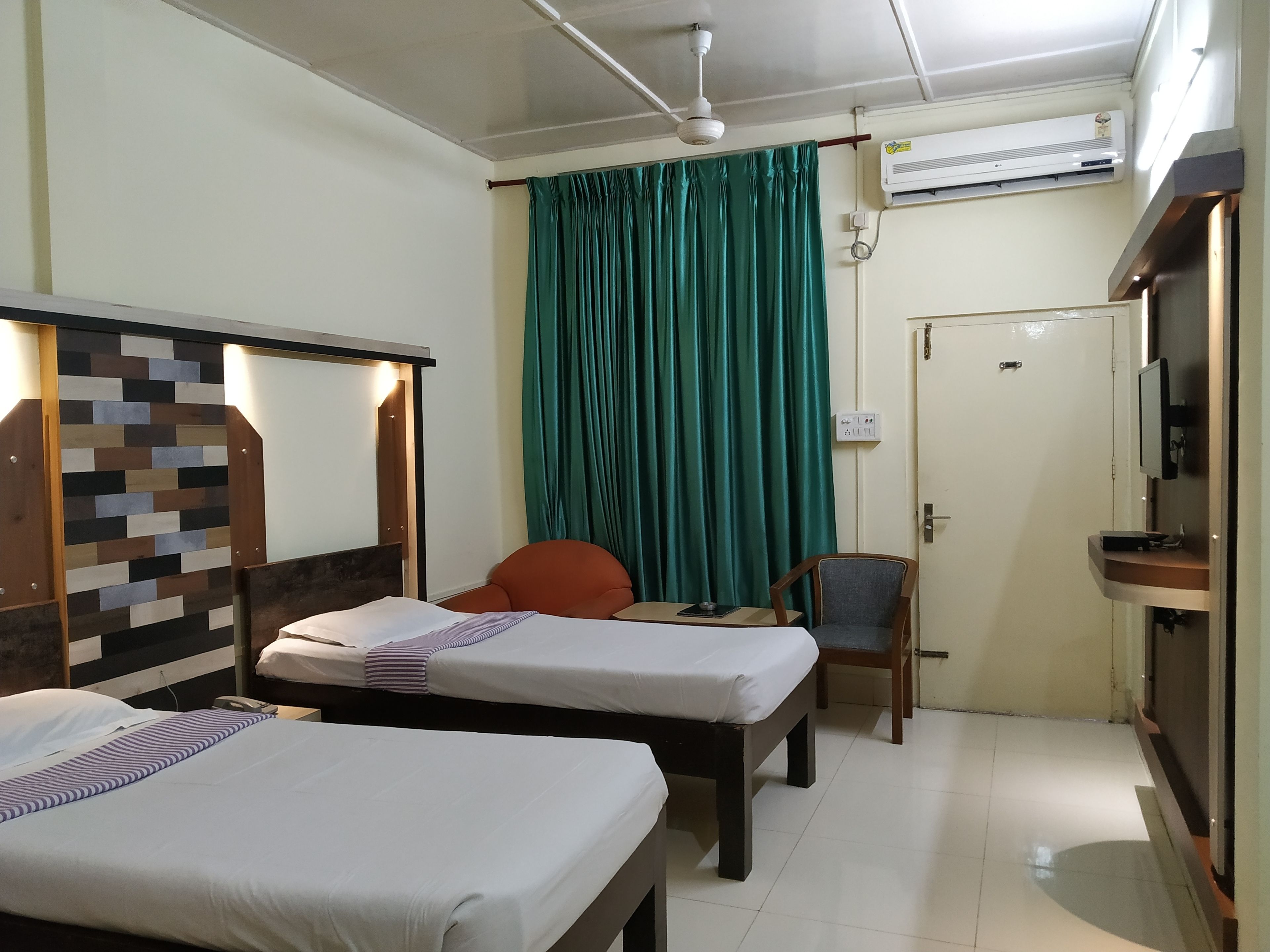 Een hotelkamer met twee enkele bedden, een bureau met stoel, een televisie en een airconditioning.