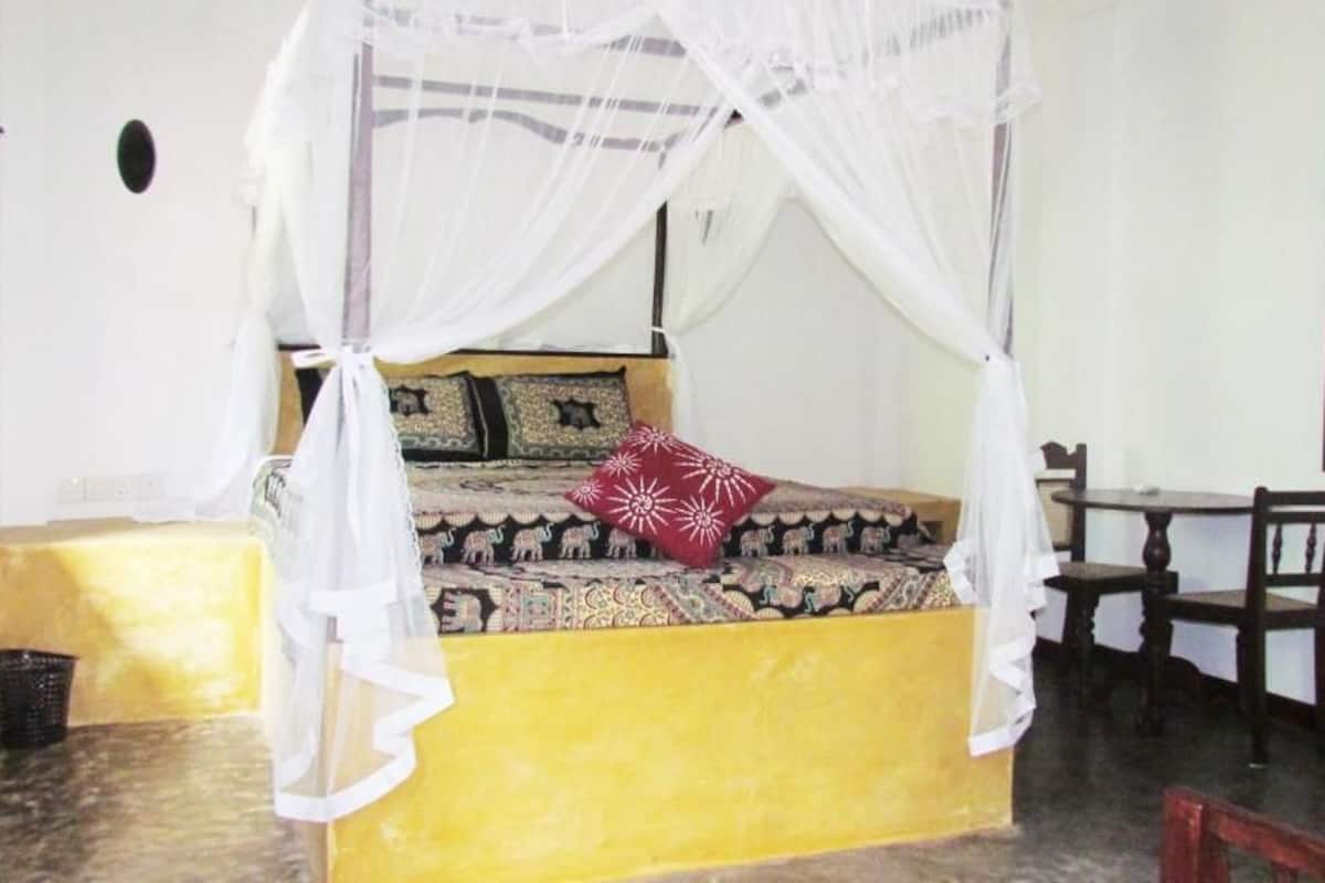 Een kamer met een bed onder een hemelbed, een tafeltje en een stoel.