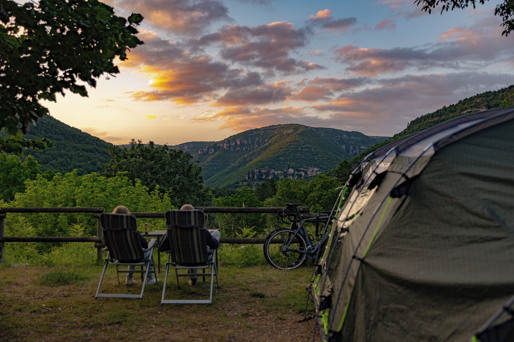 Une tente est installée, avec deux chaises placées devant, offrant une vue panoramique sur une vallée et une ville lointaine.