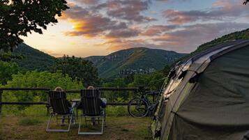 Une tente est installée, avec deux chaises placées devant, offrant une vue panoramique sur une vallée et une ville lointaine.