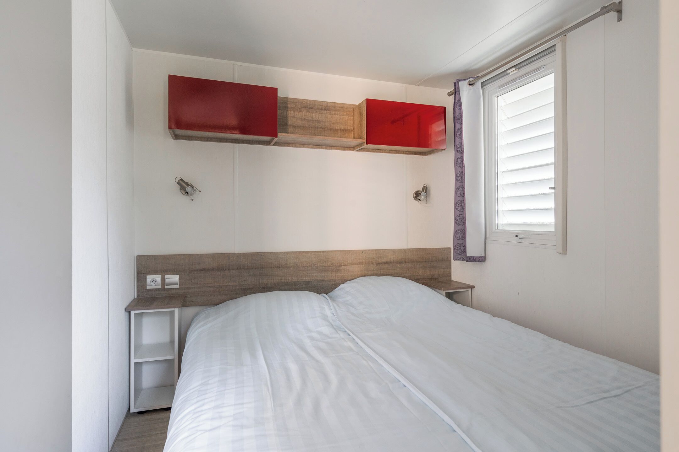 Une chambre à coucher avec un lit, une table de chevet, une tête de lit en bois et des armoires rouges au-dessus du lit.