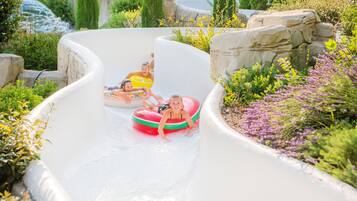 Un toboggan aquatique au design incurvé, entouré de verdure et de rochers.