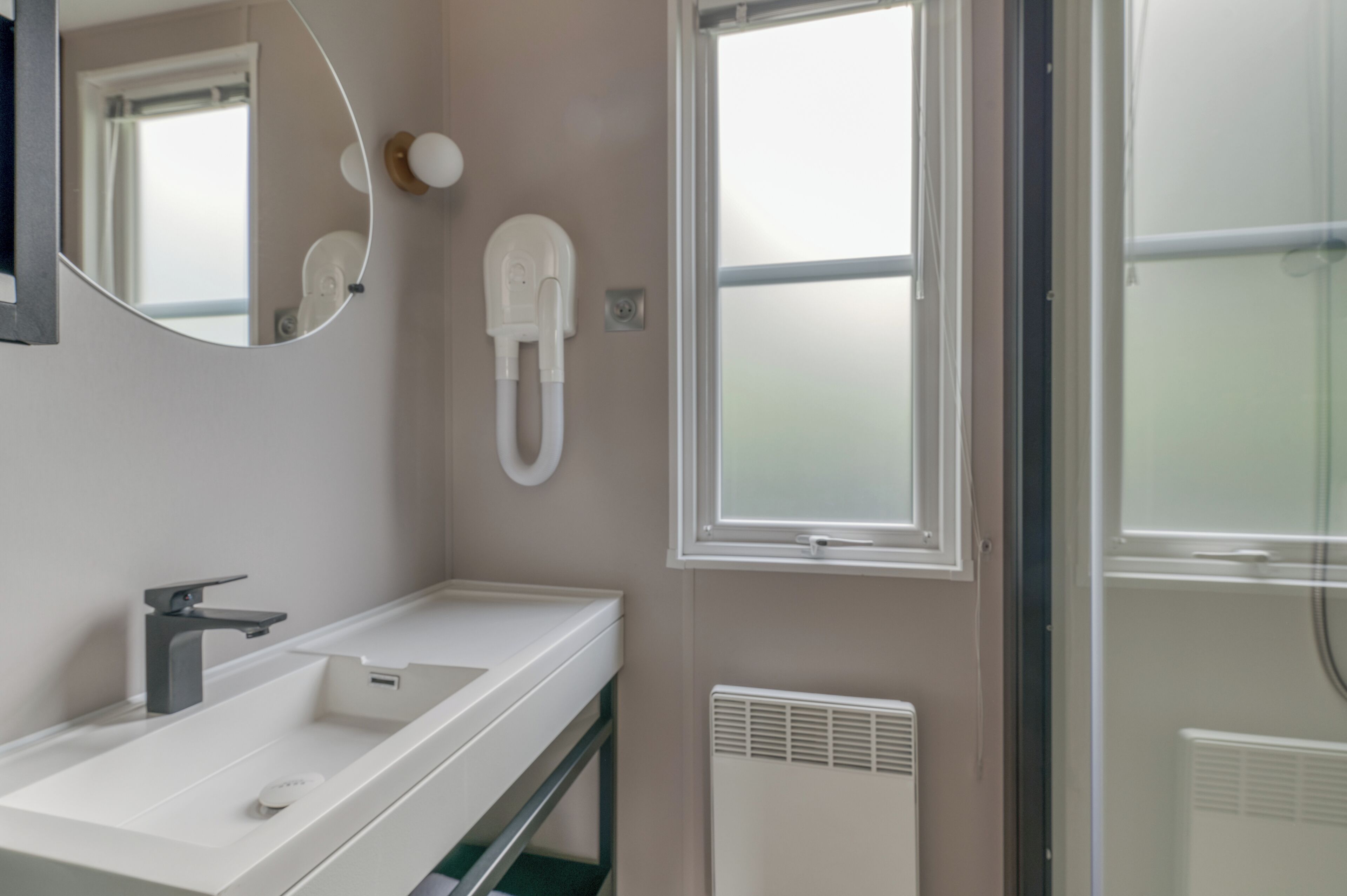 A modern bathroom with a white sink, a mirror, a telephone, and a window.