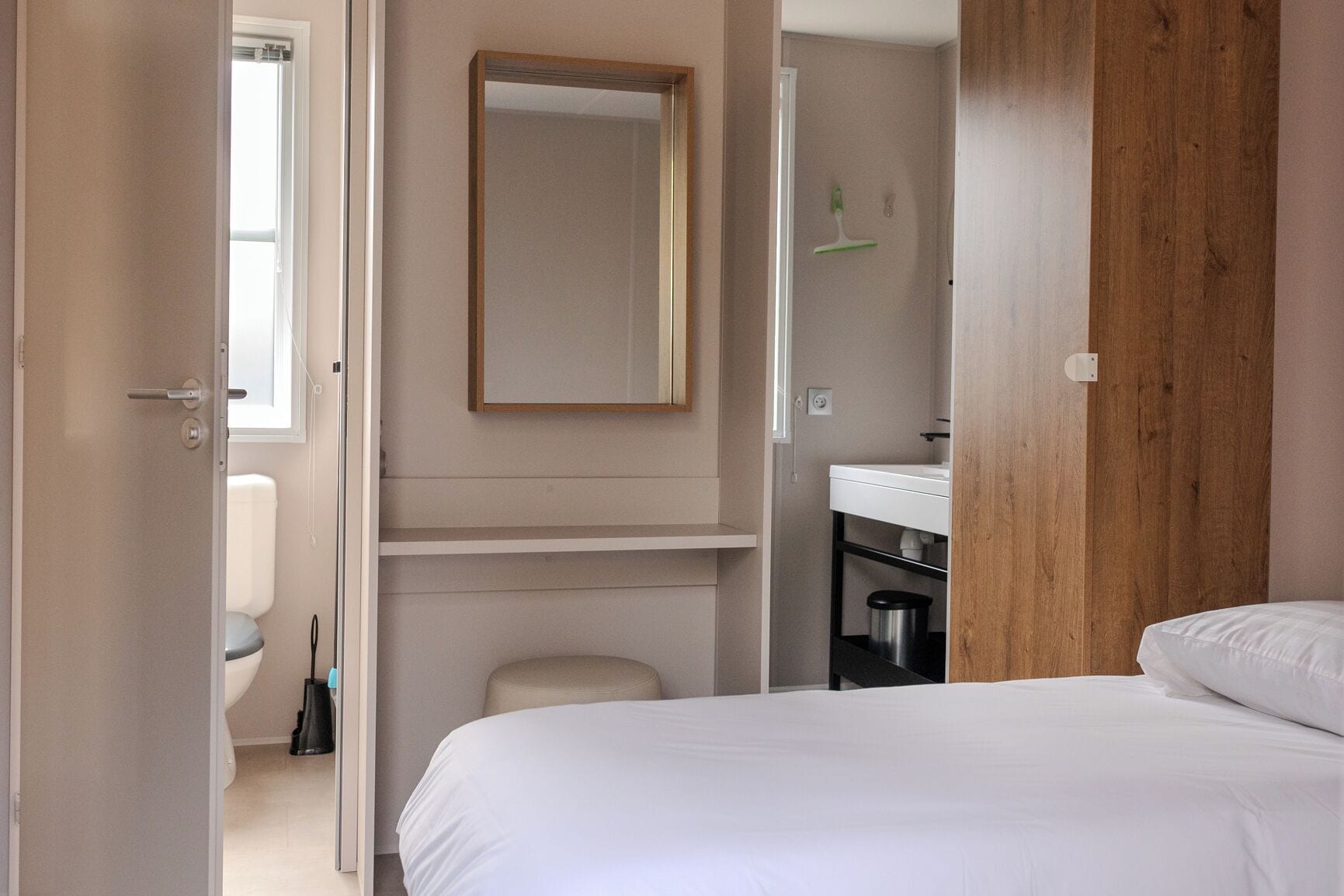 Een slaapkamer met een bed, een houten kledingkast, een badkamer met een wastafel en spiegel, en een toilet.