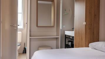 Een slaapkamer met een bed, een houten kledingkast, een badkamer met een wastafel en spiegel, en een toilet.